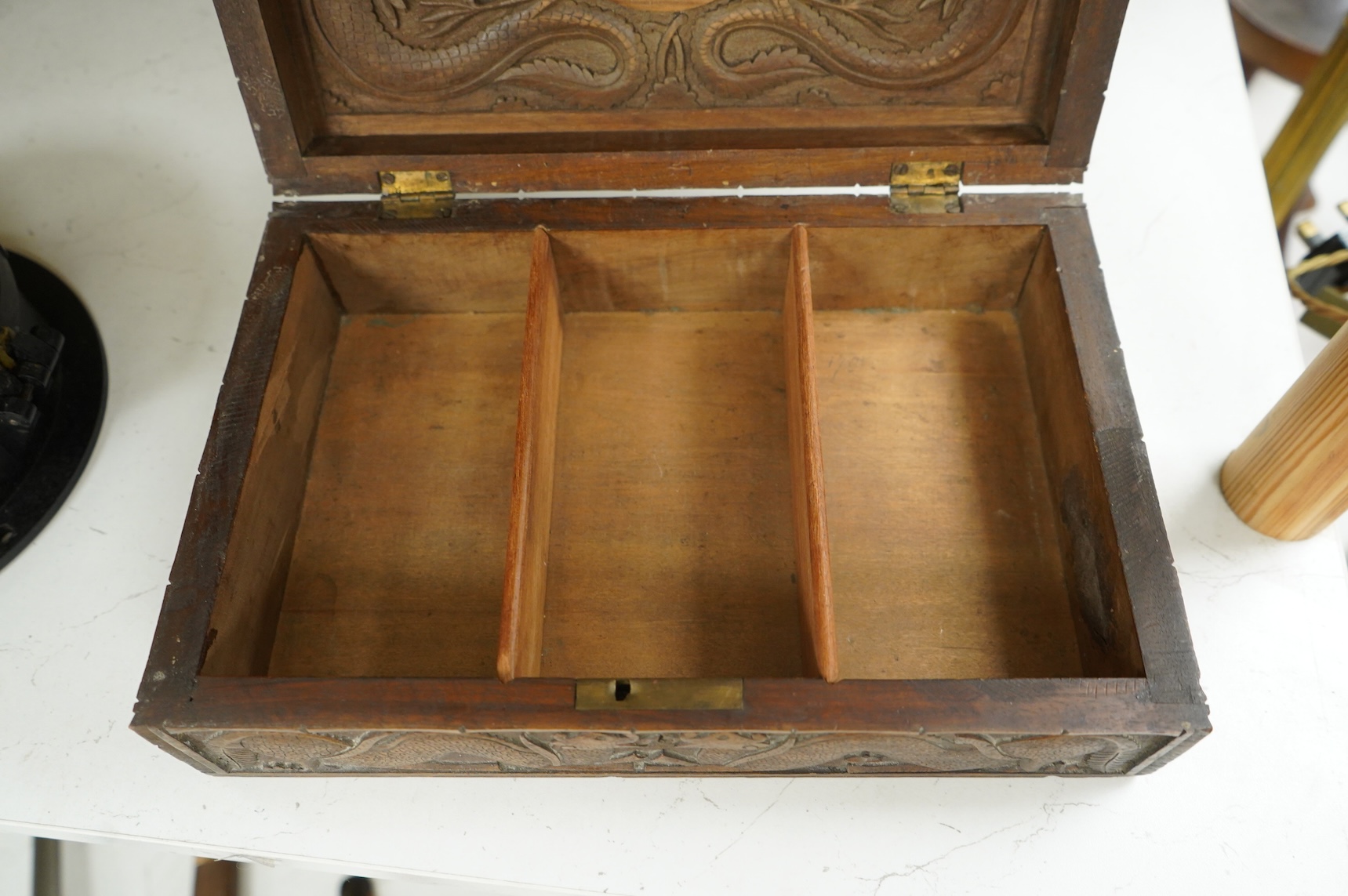 A Burmese military themed carved box, early 20th century, heavily carved with the insignia of the Devonshire Regiment to the lid, surrounded by mythical dolphins, serpents, and geometric patterns, with segmented interior